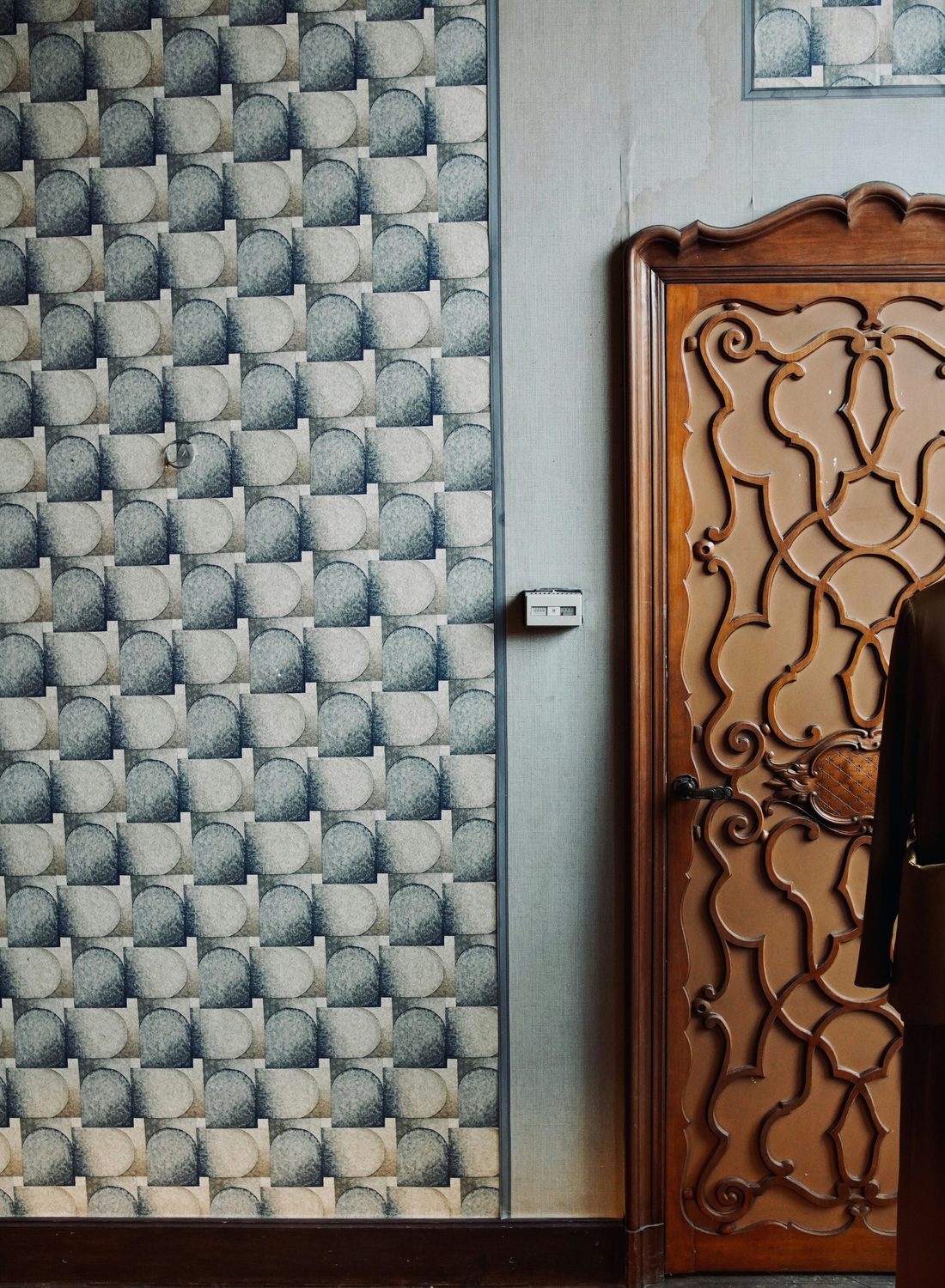 Grey-blue geometric arch-motif wallpaper beside a carved wooden door