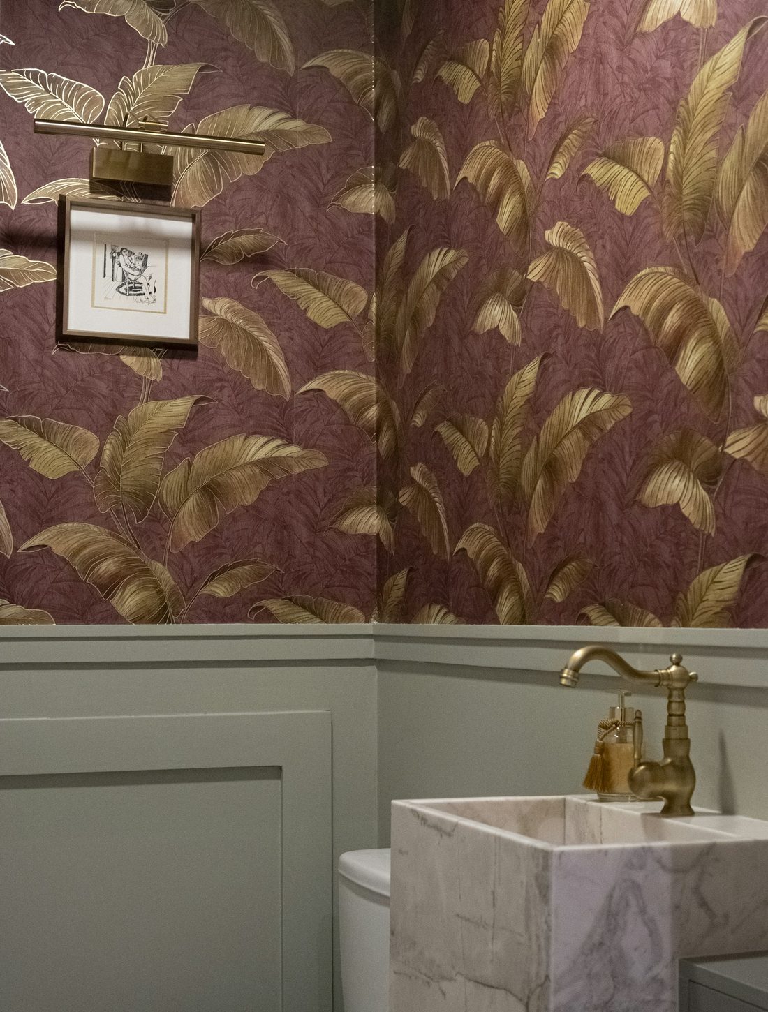 Burgundy and gold banana-leaf wallpaper above sage wainscoting in a powder room
