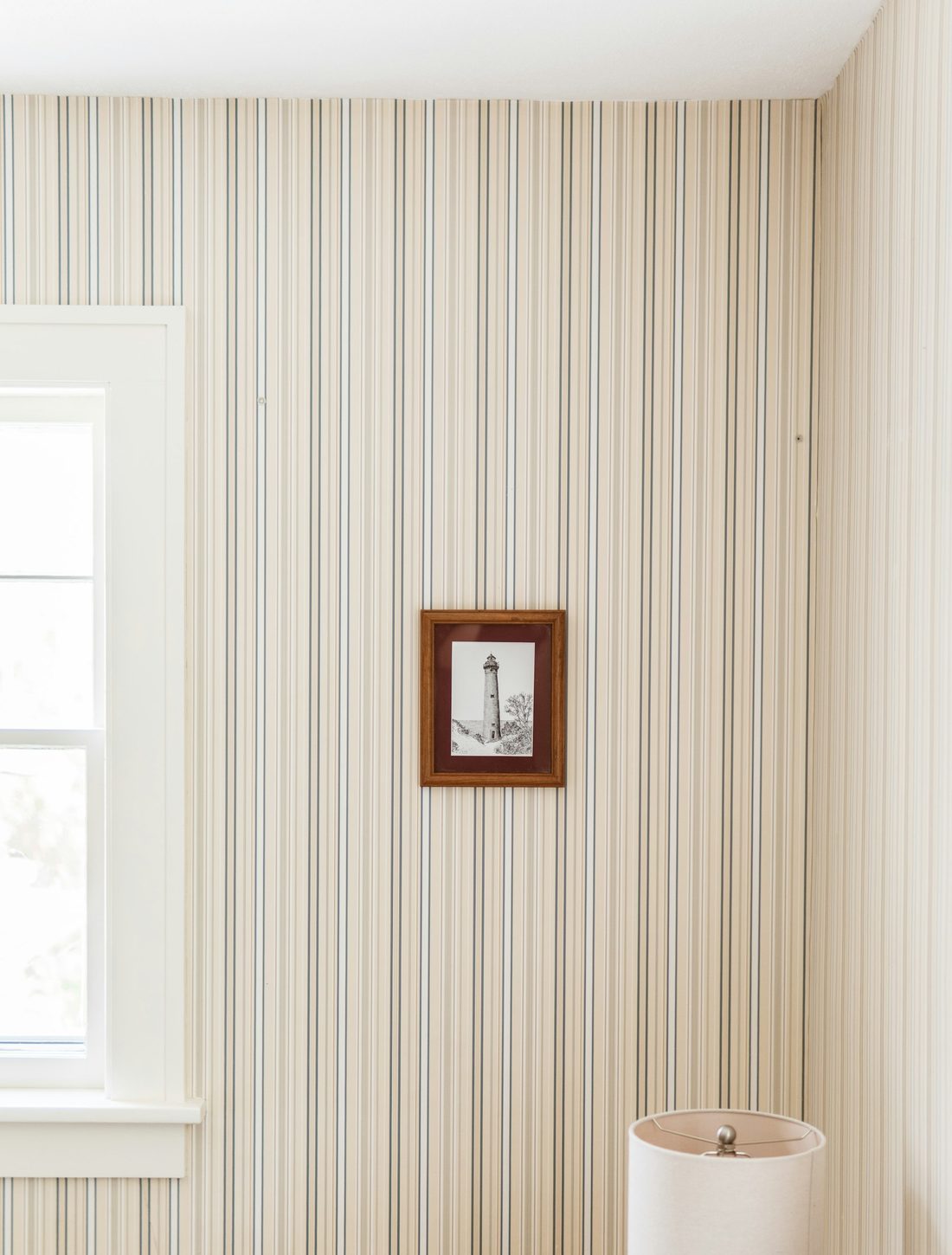 Soft cream pinstripe wallpaper beside a window in a calm bedroom